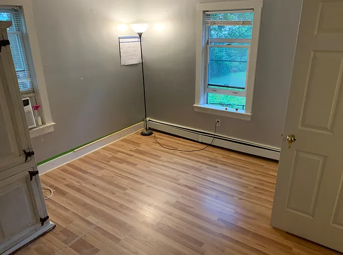A room with hardwood floors, a lamp, and a window.