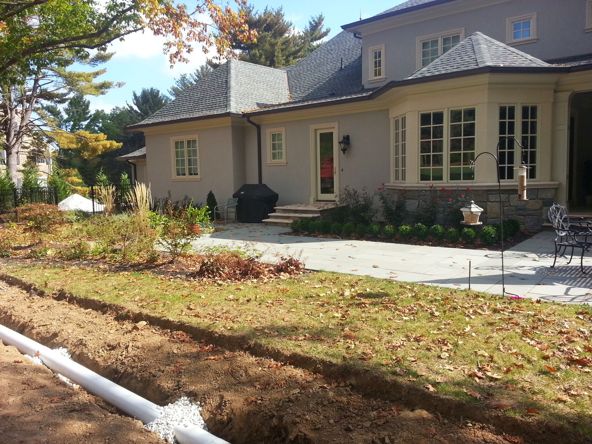 Suburban house with a stone patio, front garden, and autumn leaves along the lawn edge