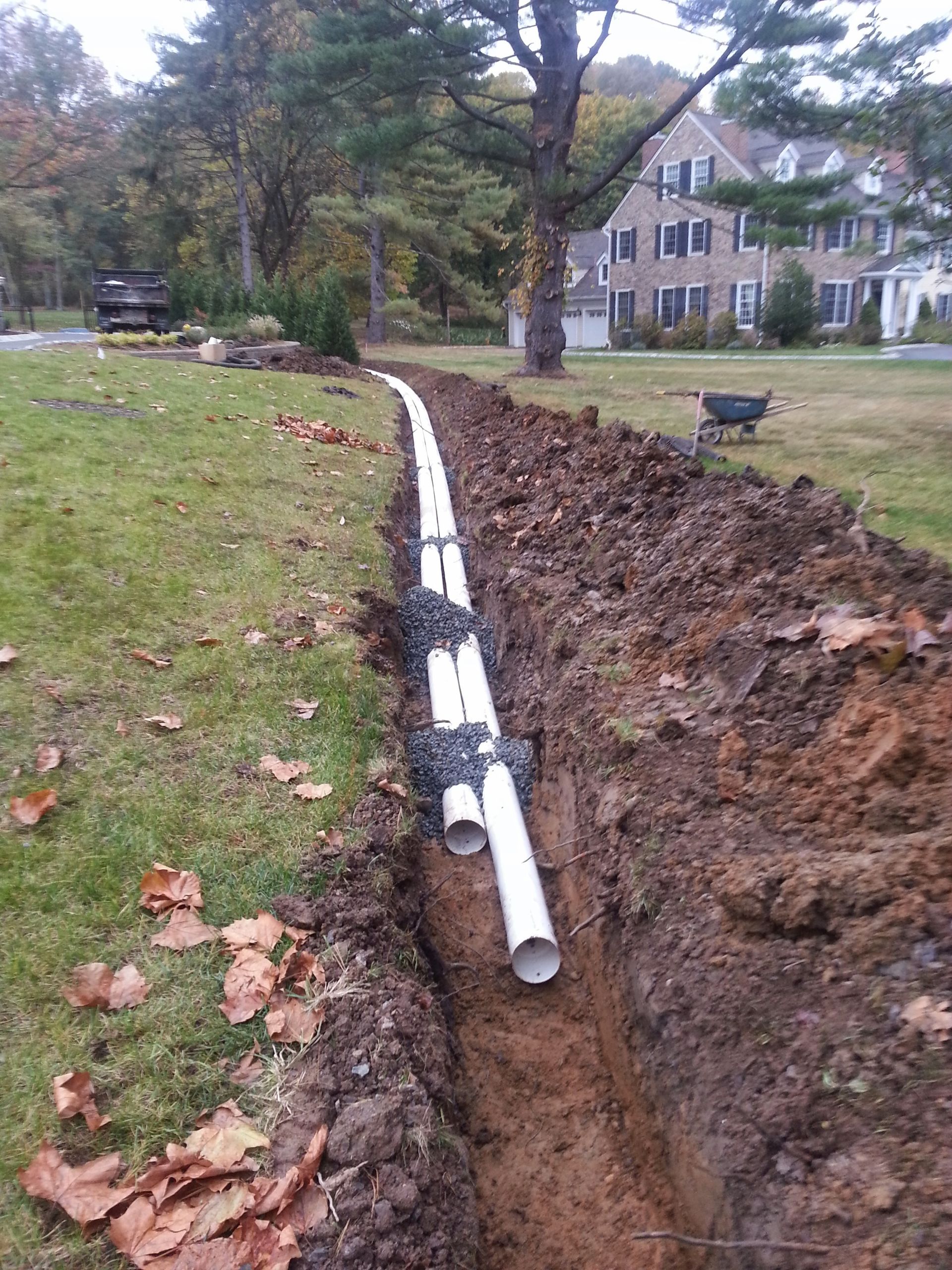 Trenched yard with a white pipe laid in the ground beside a grassy lawn and house