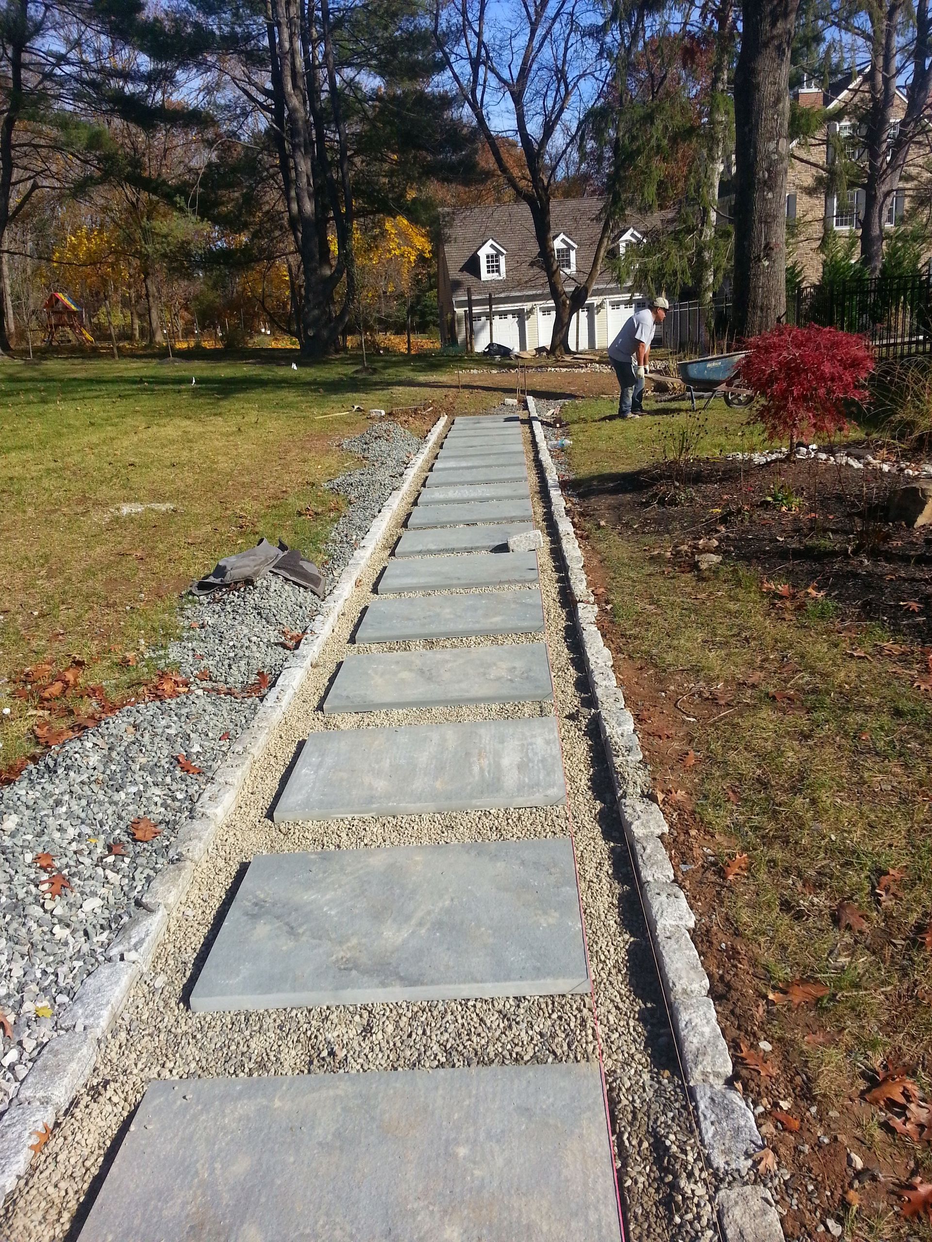 Stone path through autumn yard leading to a white house, with two people in the distance.
