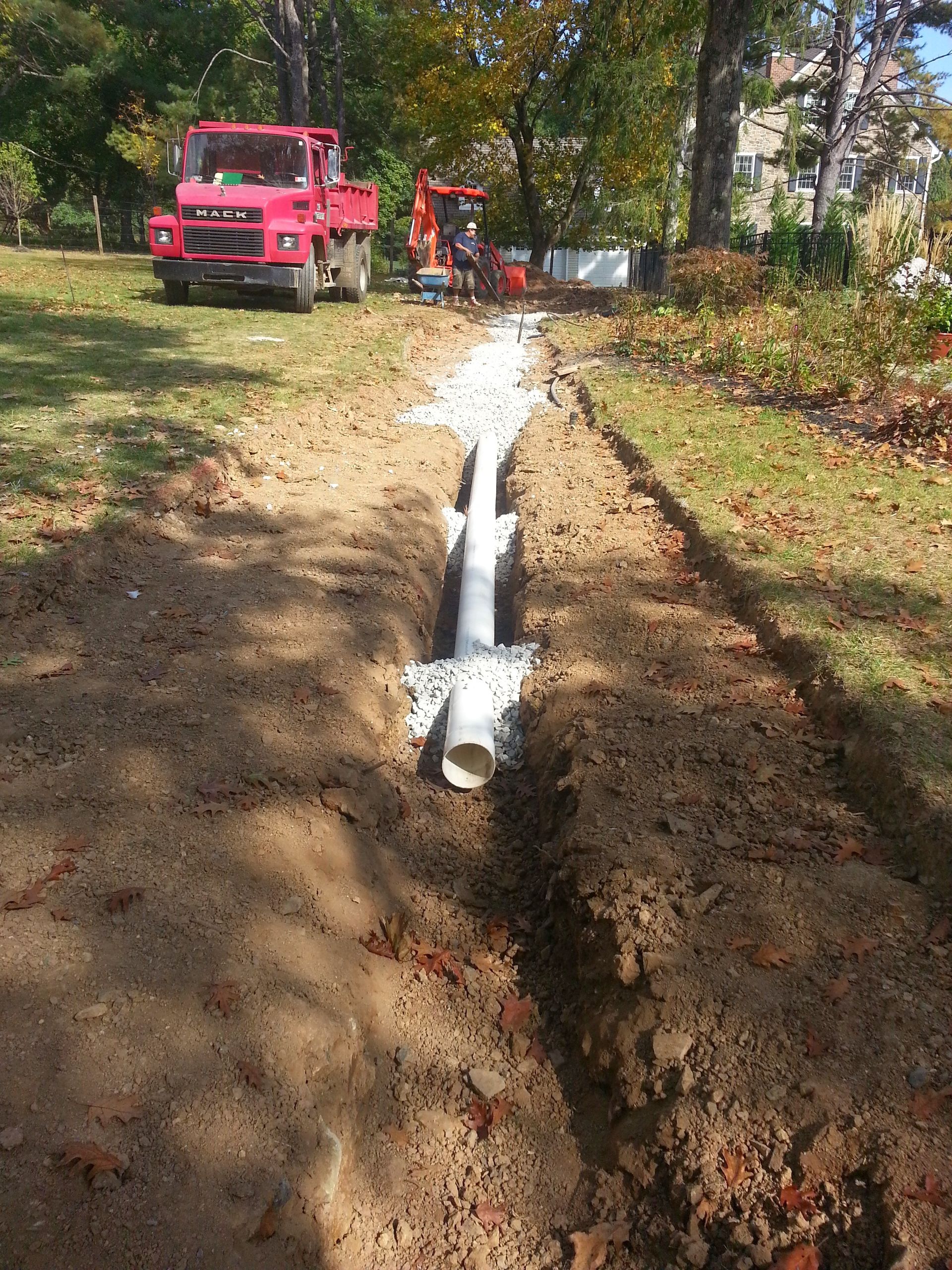 Red utility truck on a dirt road beside a white pipe trench in a wooded worksite
