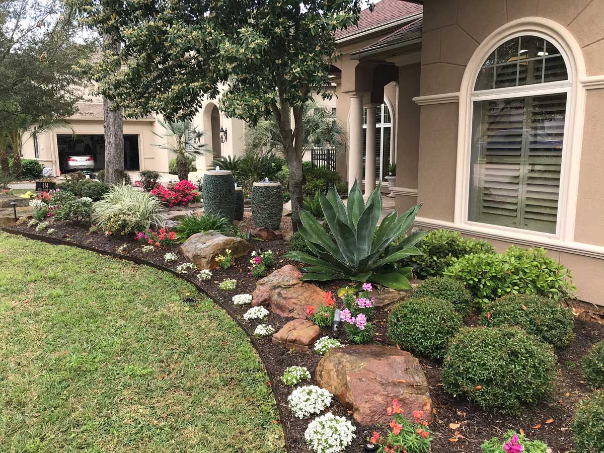 Landscaped front yard with tan house, green lawn, and a variety of plants, including flowers and succulents.