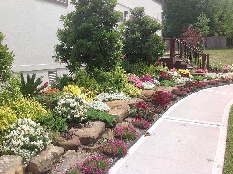 Colorful flower bed with large rocks next to a sidewalk and house.