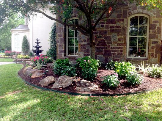 Stone house with arched windows, lush landscaping, and a tiered fountain in the background.