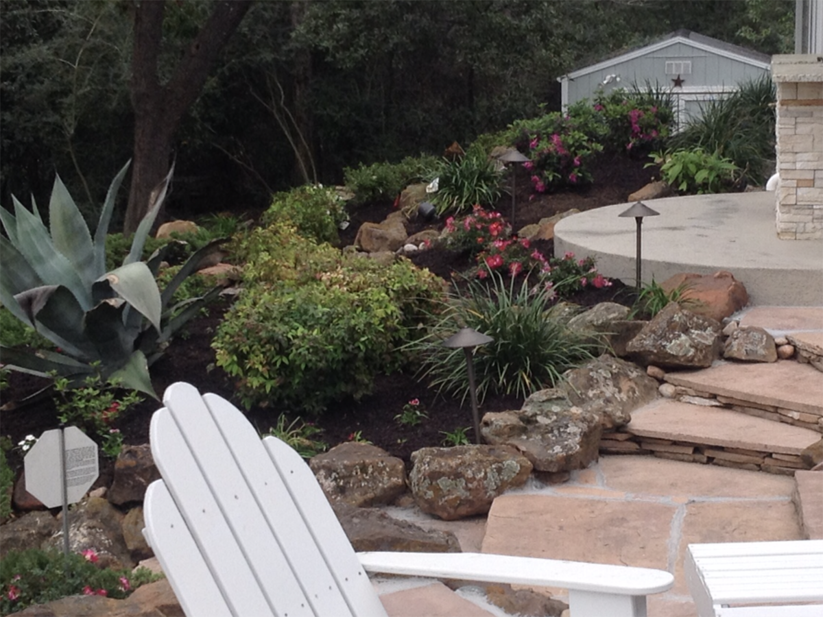 Landscaped yard with stone steps, plants, and white chairs; a shed in the background.