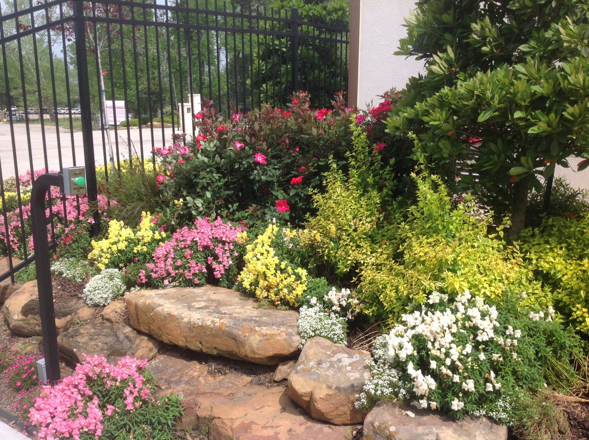 Colorful flower bed with rocks and bushes in front of a black fence.