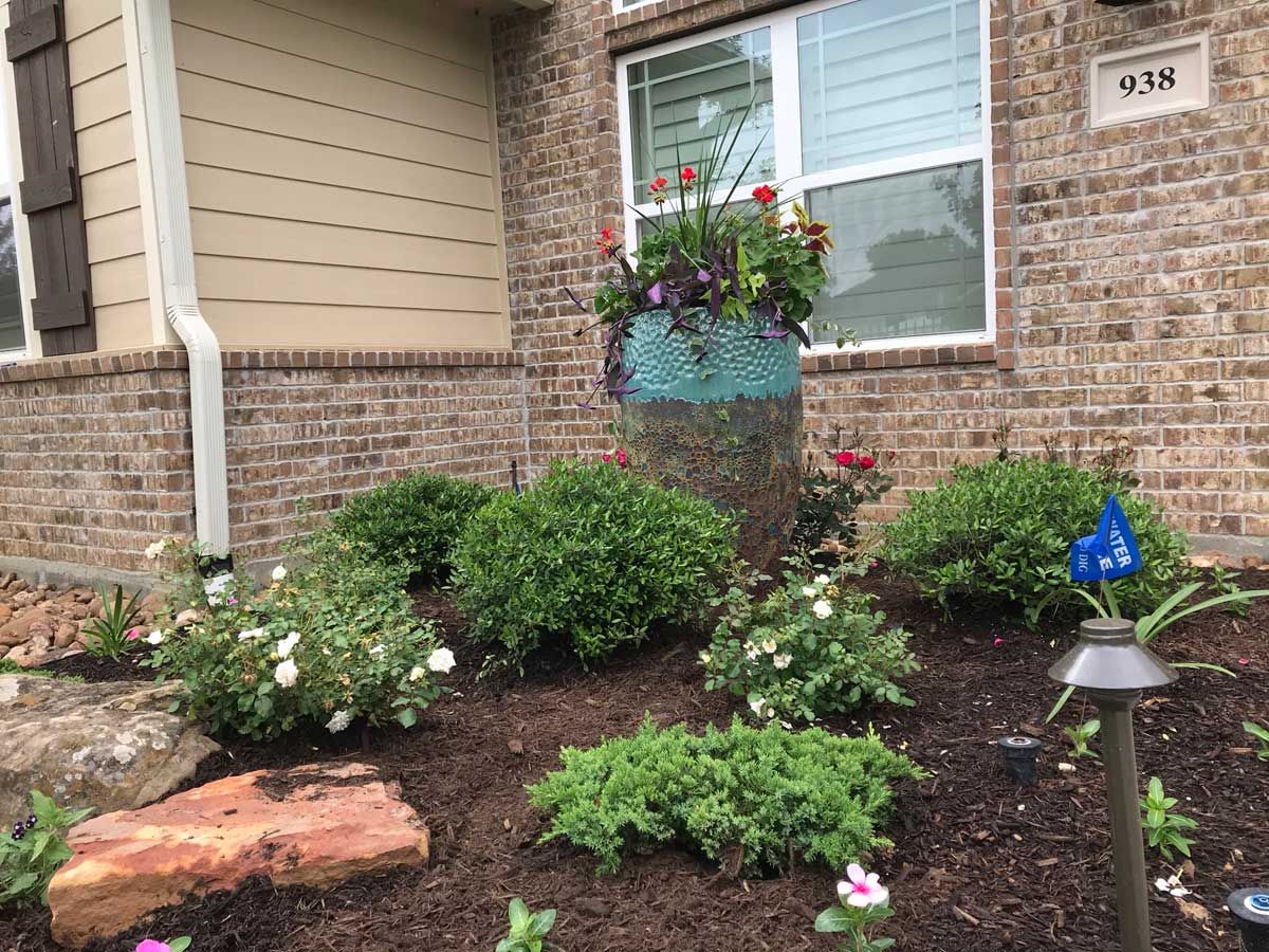 Brick house with a flower pot, bushes, mulch, and a rock, with the number 938 visible.