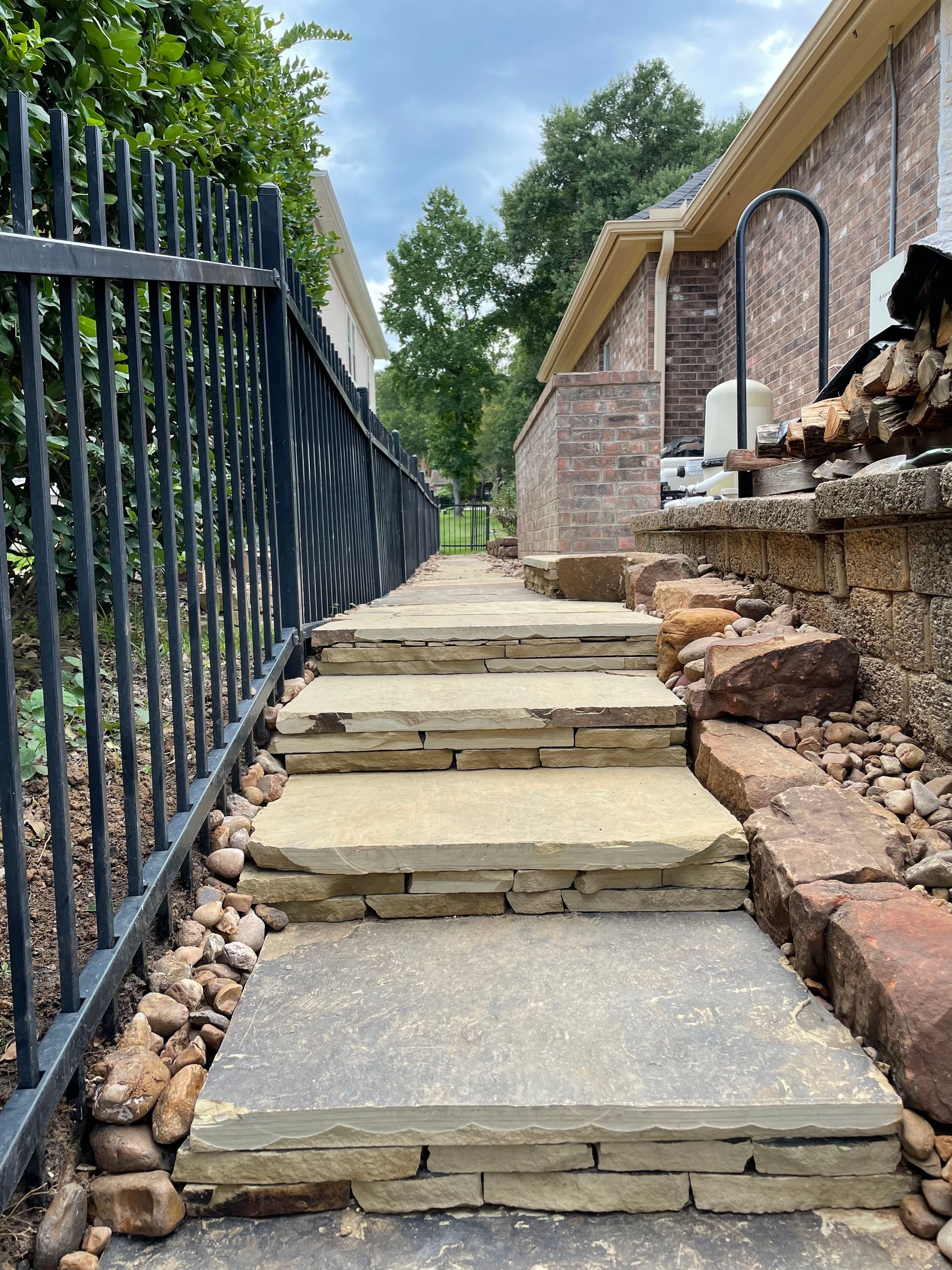 Stone steps and walkway beside black metal fence and brick house.