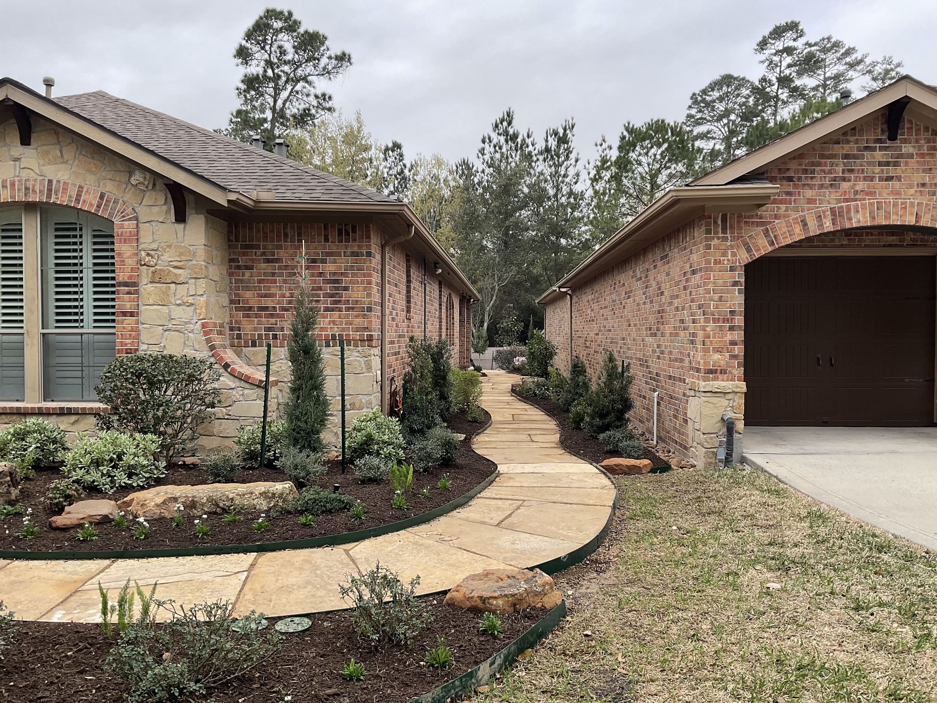 Brick homes with arched garage entrance and stone pathway. Lush landscaping with trees.