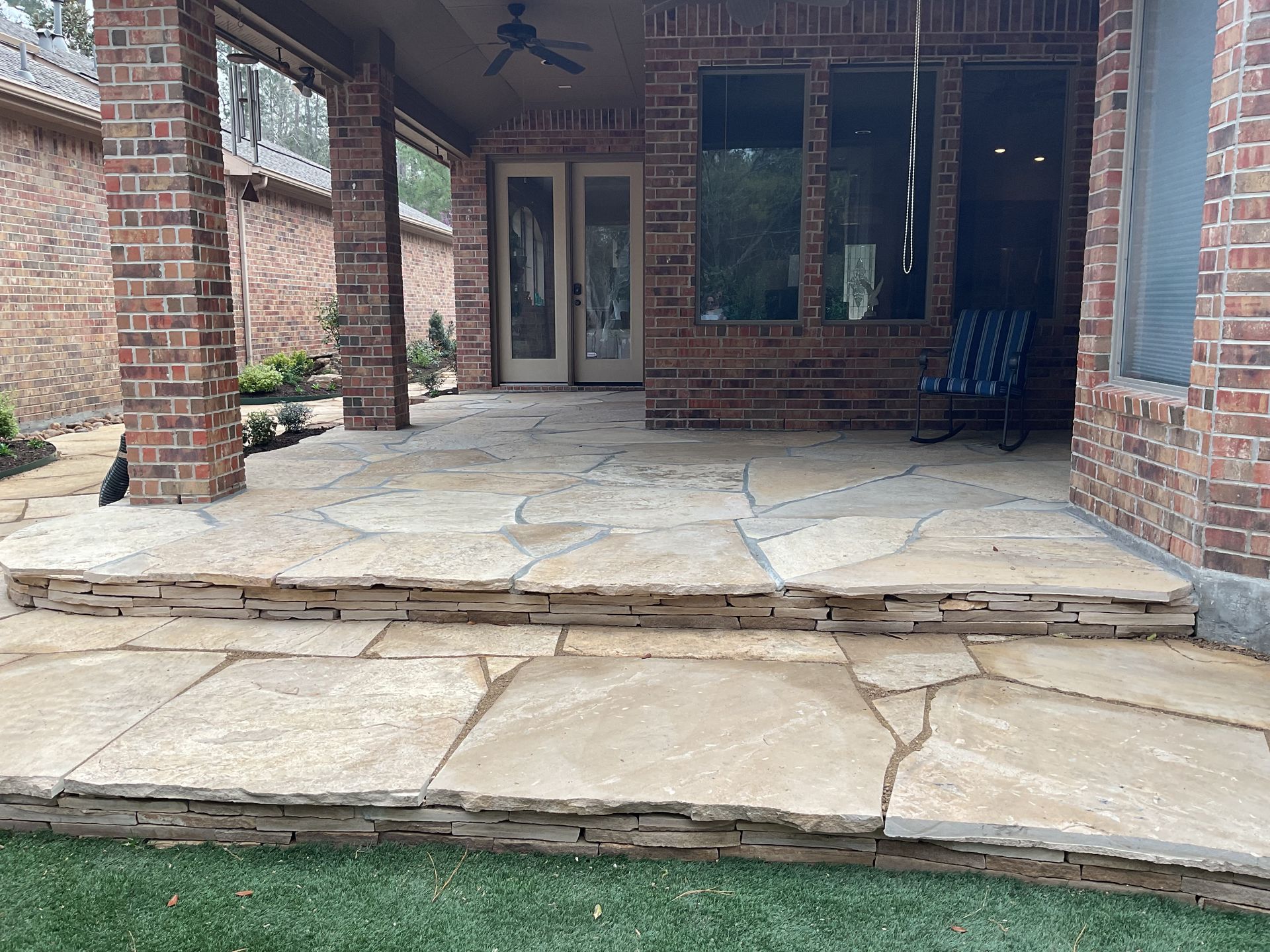 Stone patio with steps, brick columns, and lawn.