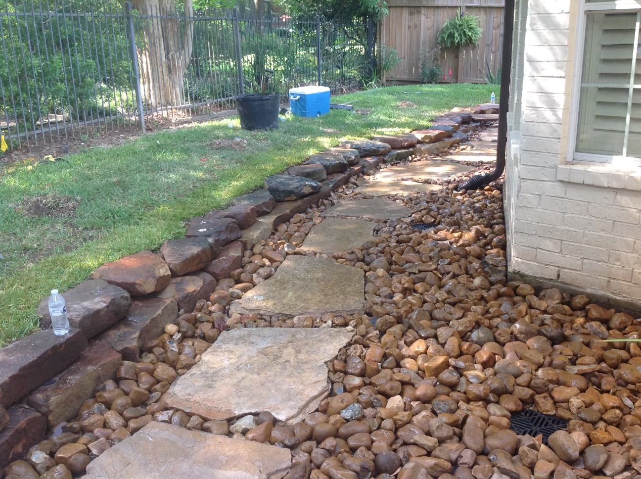Stone pathway with large rocks alongside a house and grassy area.