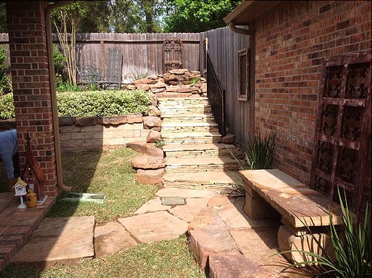 Stone steps leading up a tiered garden with brick walls and a wooden fence.