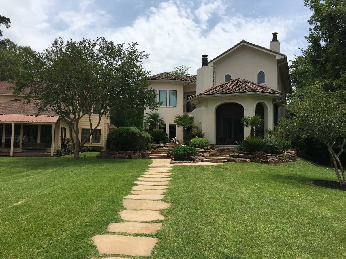 Large cream-colored house with terracotta roof. Stone path leads through green lawn. Sunny day.