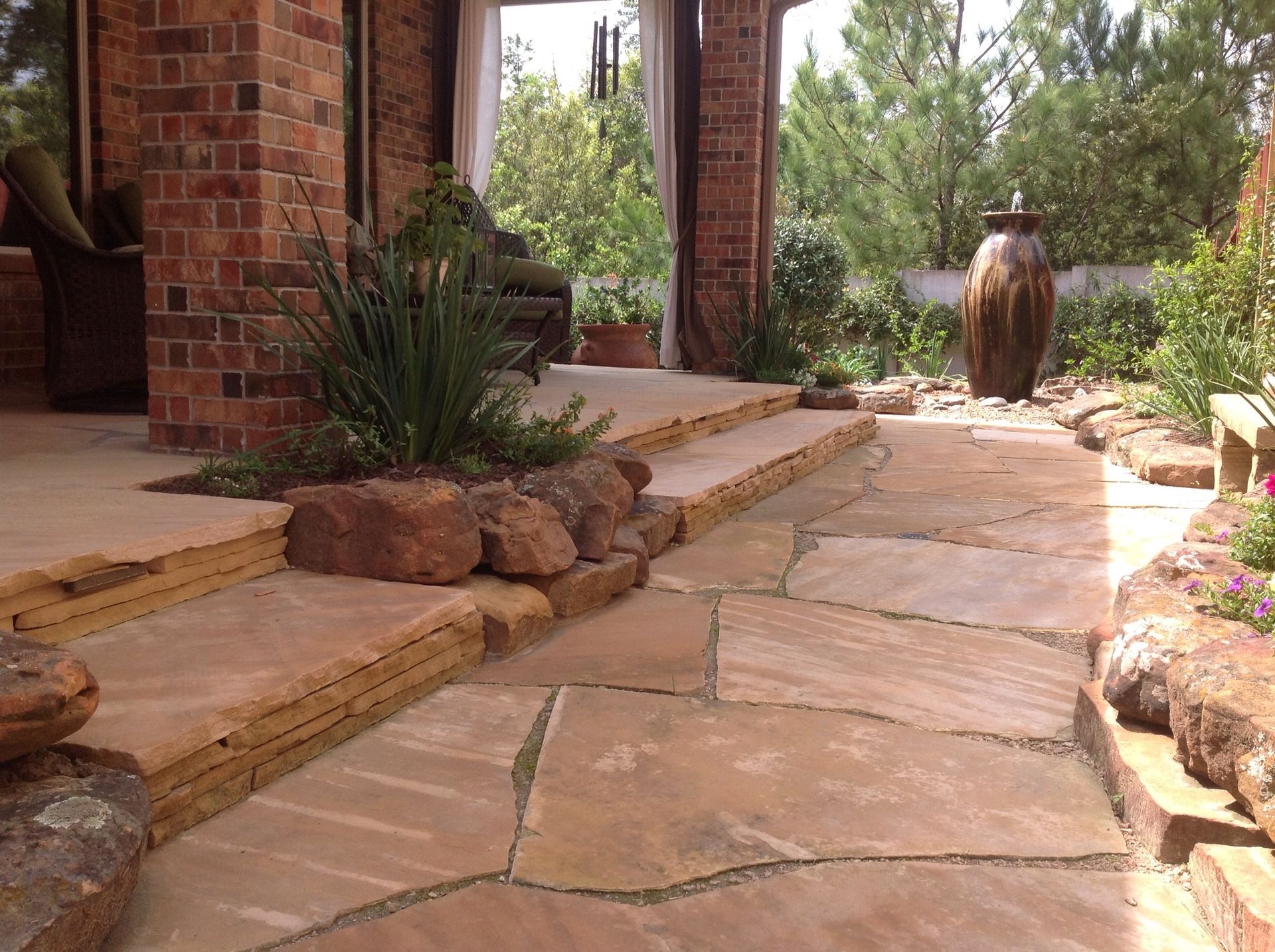 Stone patio with steps, landscaping, and a fountain. Red brick building on the left.