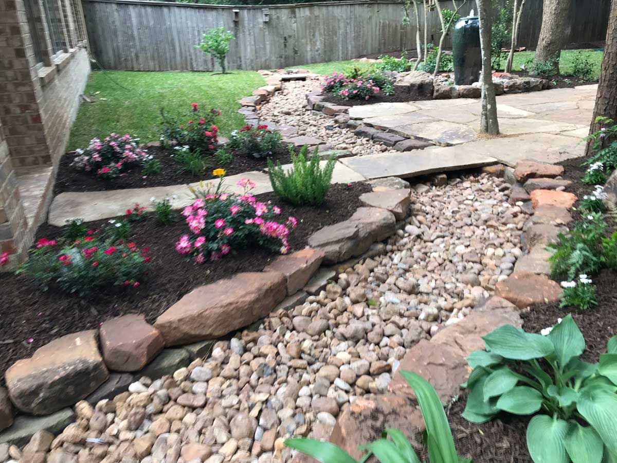 Landscaped backyard with a dry creek bed, stone pathway, and flowering plants.
