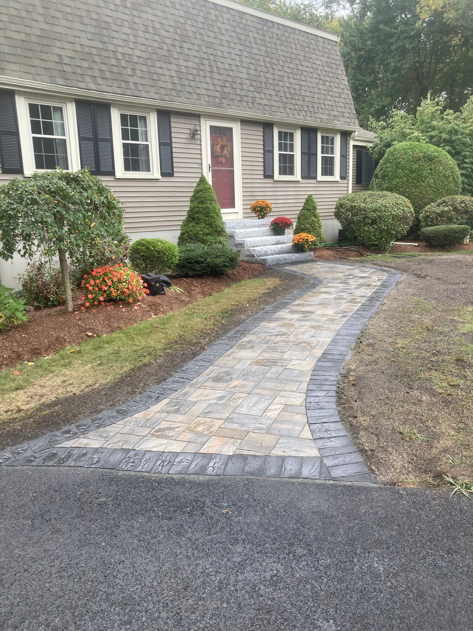 Stone walkway leading to a home's front door, flanked by bushes and flower arrangements.