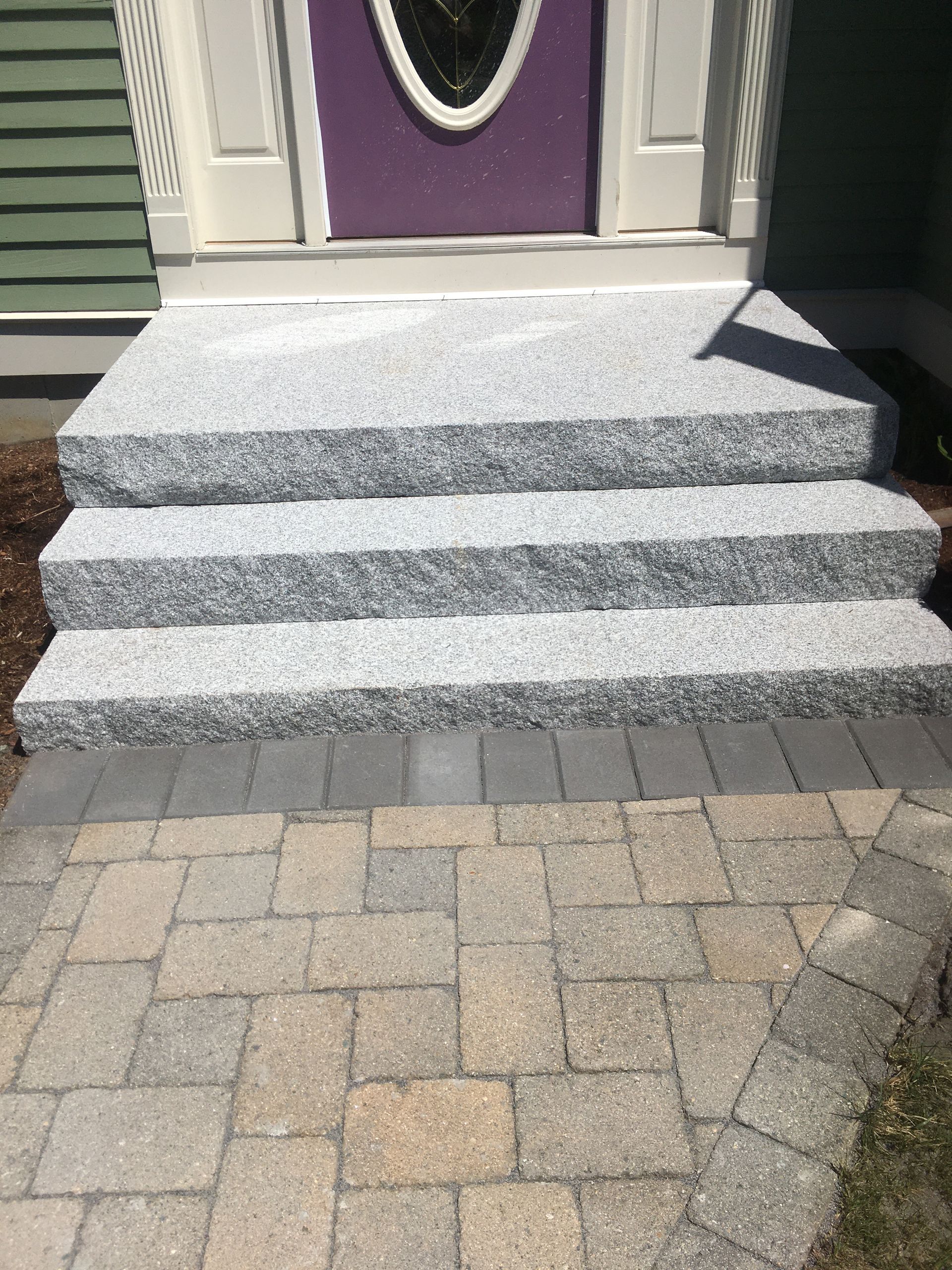 Granite steps leading to a purple door; a brick pathway in front.