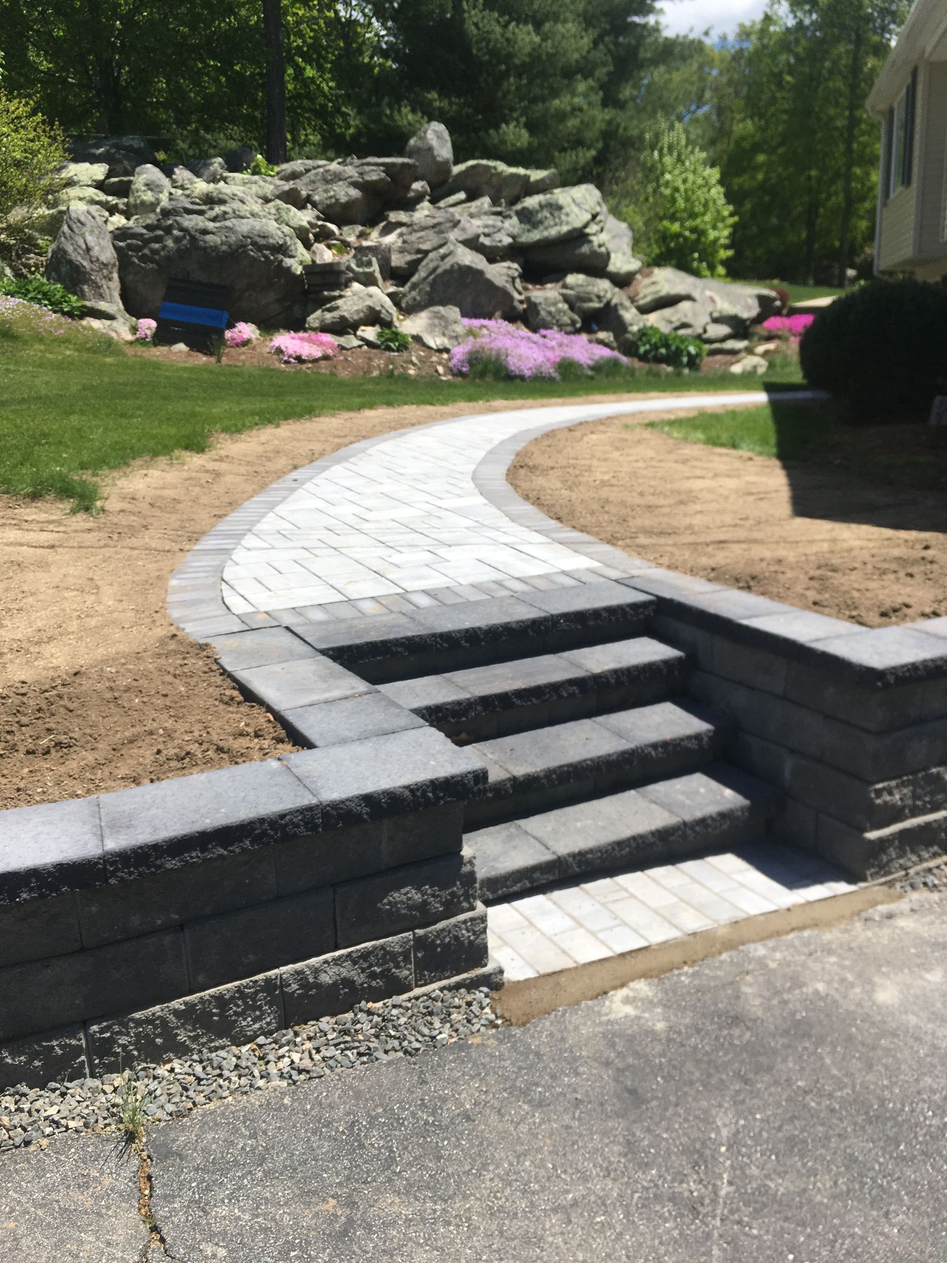 Stone steps and walkway leading to a rock garden. Grey pavers, retaining walls, and green grass.