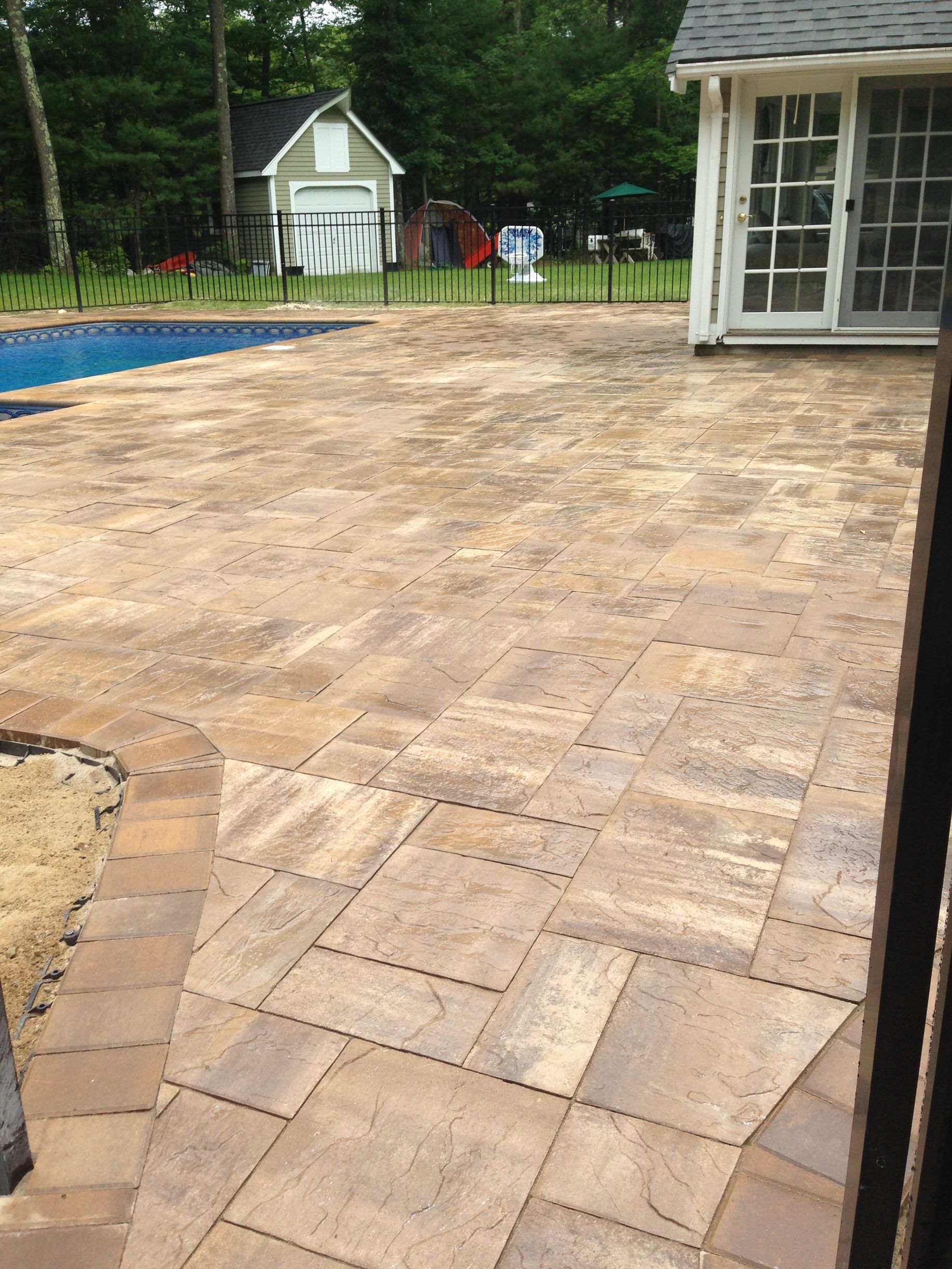 Patio with rectangular paving stones, pool, and a white building in the background.