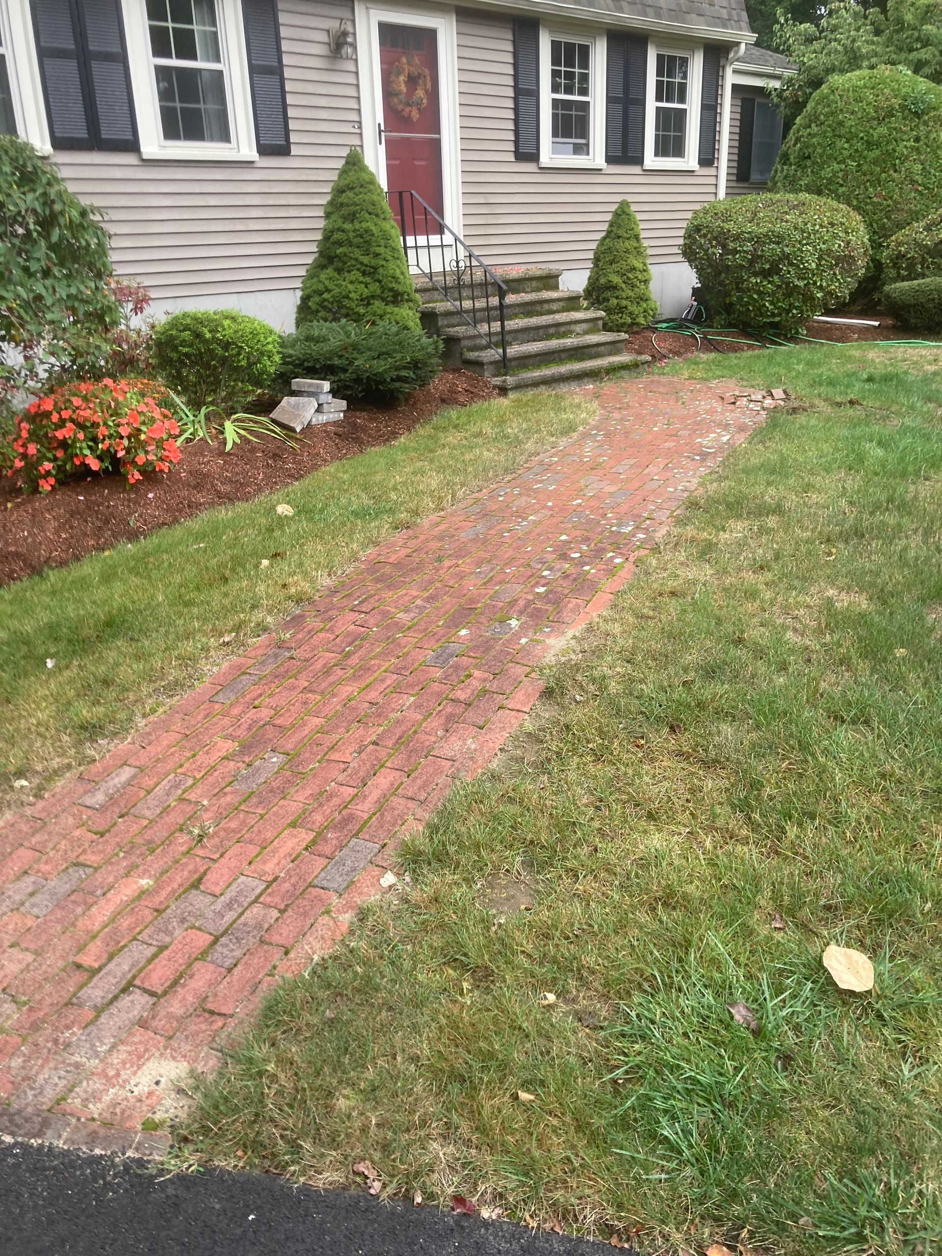 Brick path leads to house with shrubs and flowerbed.
