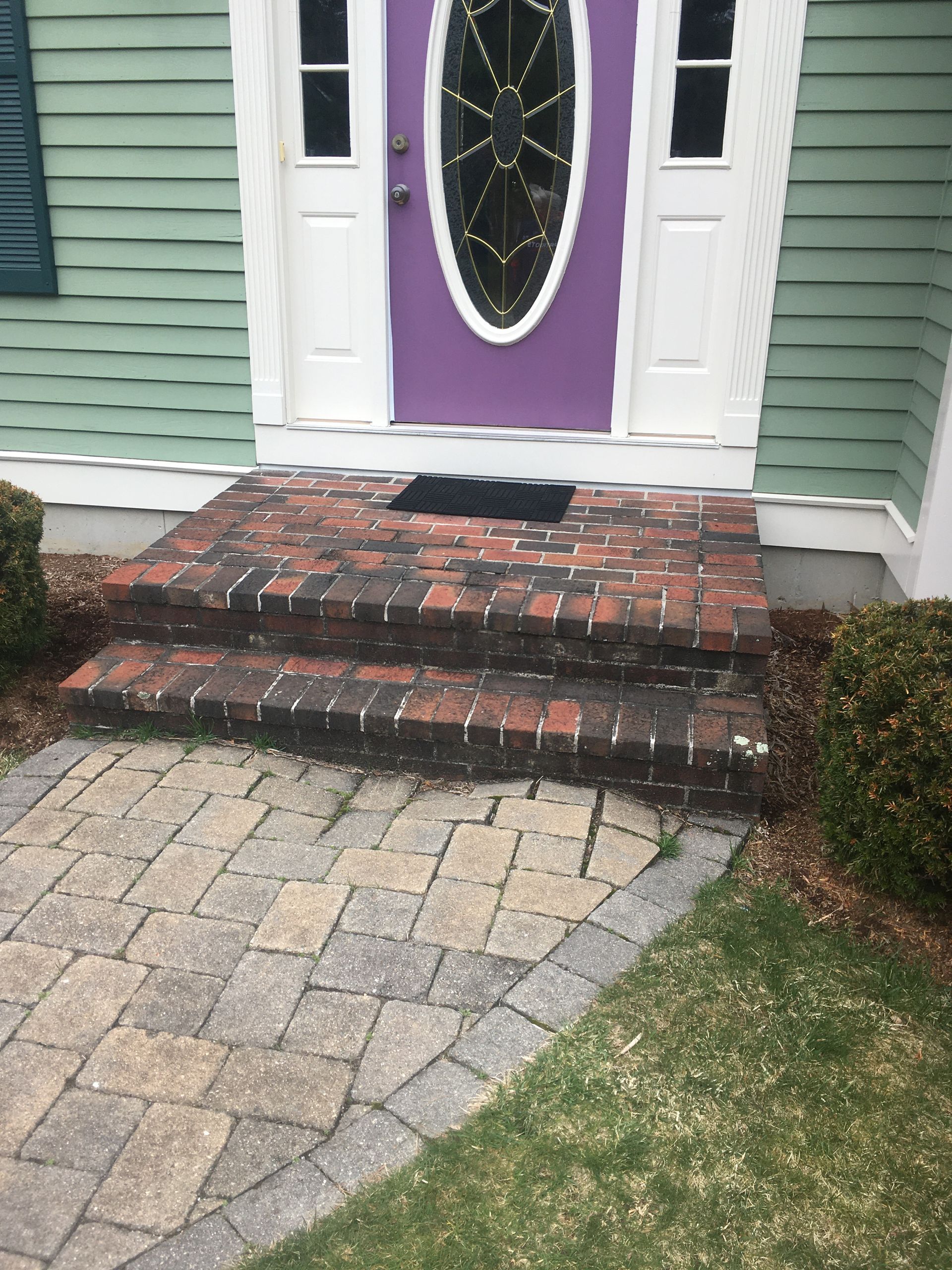 Brick steps lead to a purple front door with an oval window. A brick and stone path leads to the steps.