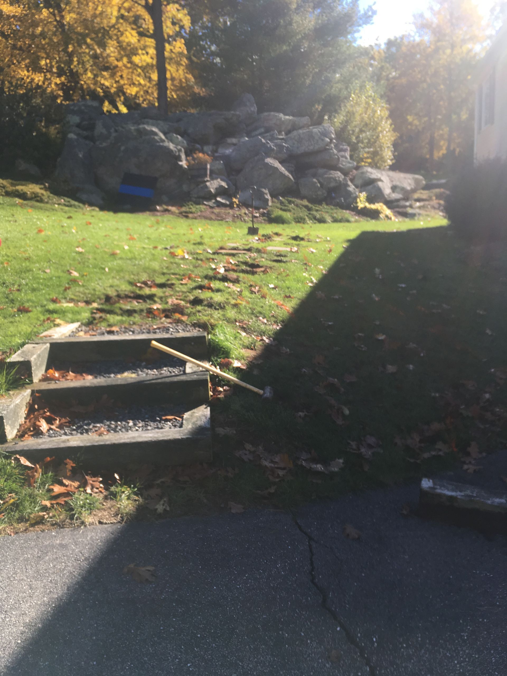 Stone steps lead to a grassy area with a rock pile. Yellow leaves in background.