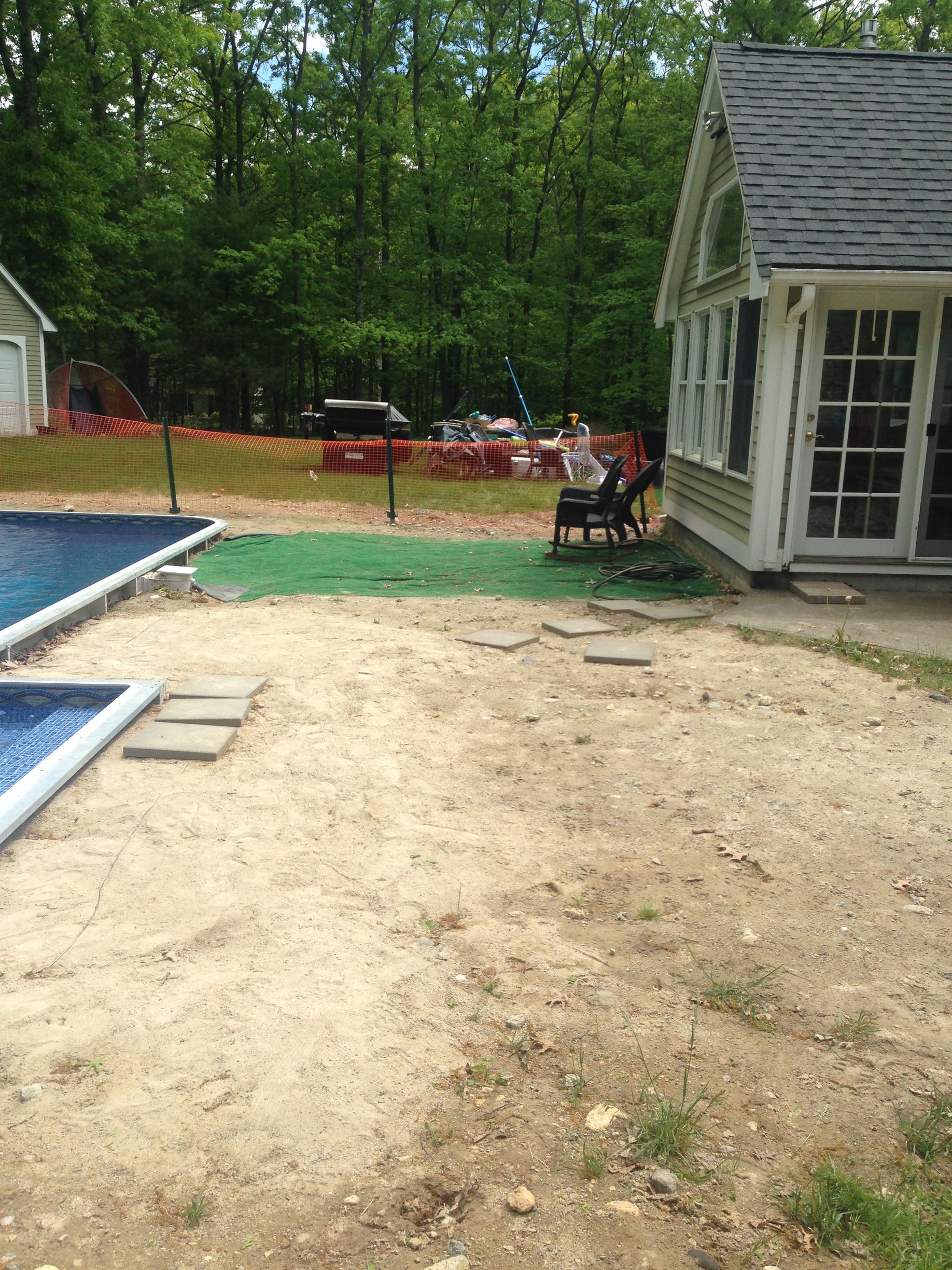 Sandy yard with pool and sunroom, trees in background. Person seated in chair.
