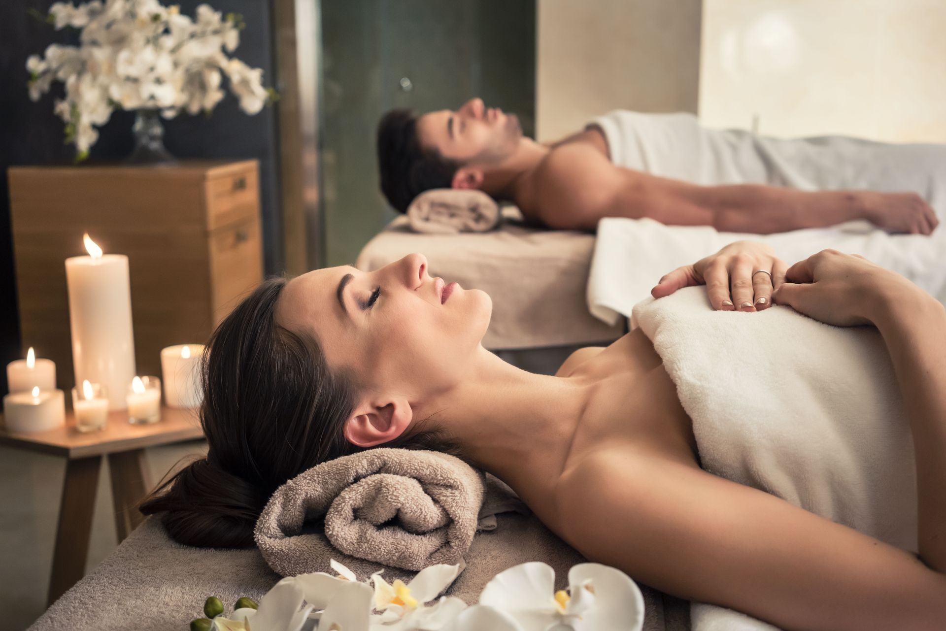 Couple relaxing on massage tables at a spa. Candles and flowers on side table.