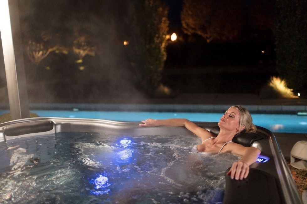 A woman is laying in a hot tub next to a pool at night.