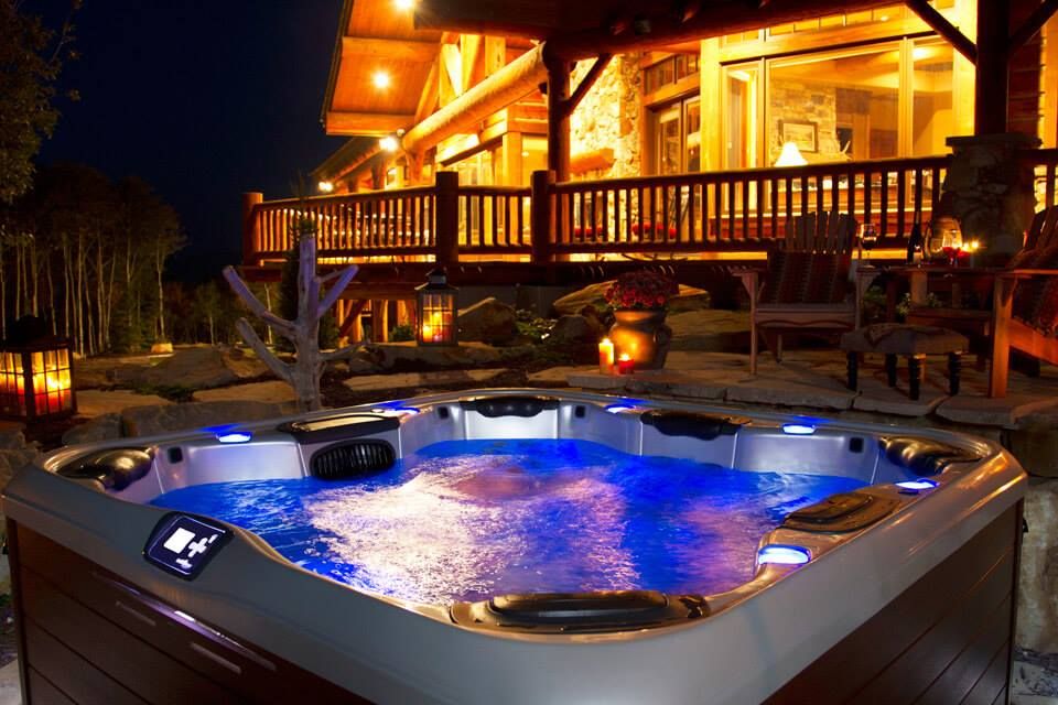A hot tub is lit up at night in front of a log cabin.