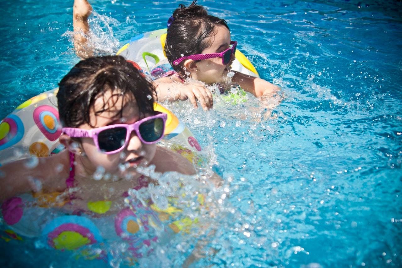 Two young girls wearing sunglasses are swimming in a pool.