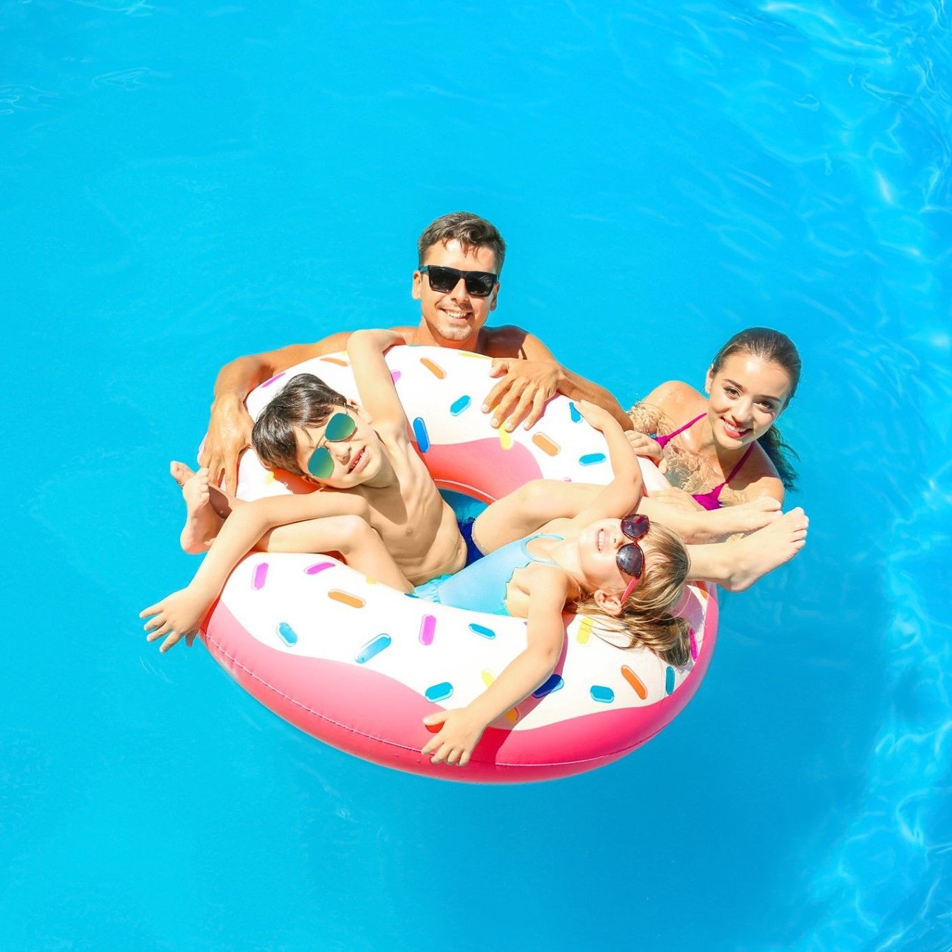 A family is floating on a donut float in a swimming pool.