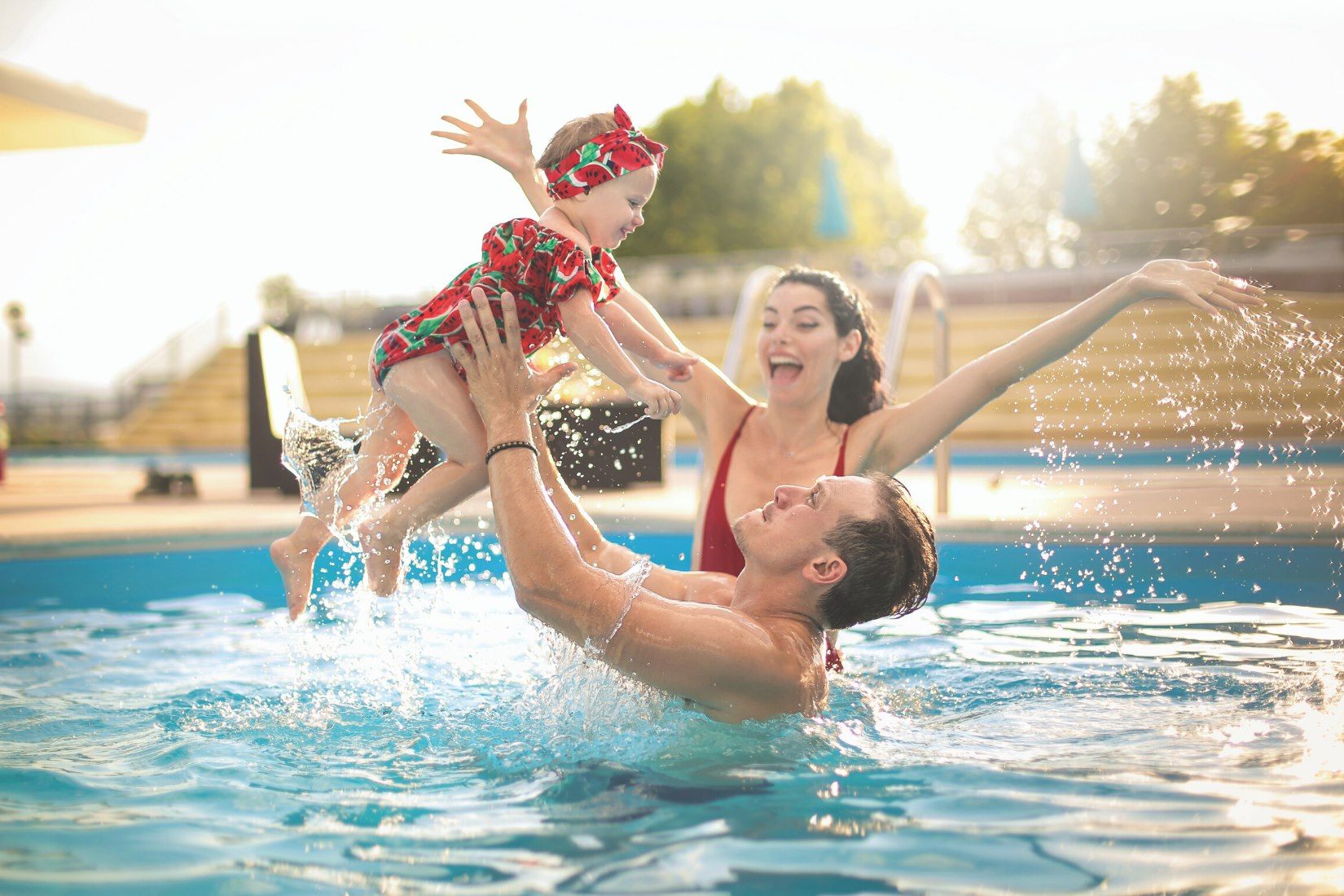 A man is holding a little girl in the air in a swimming pool.
