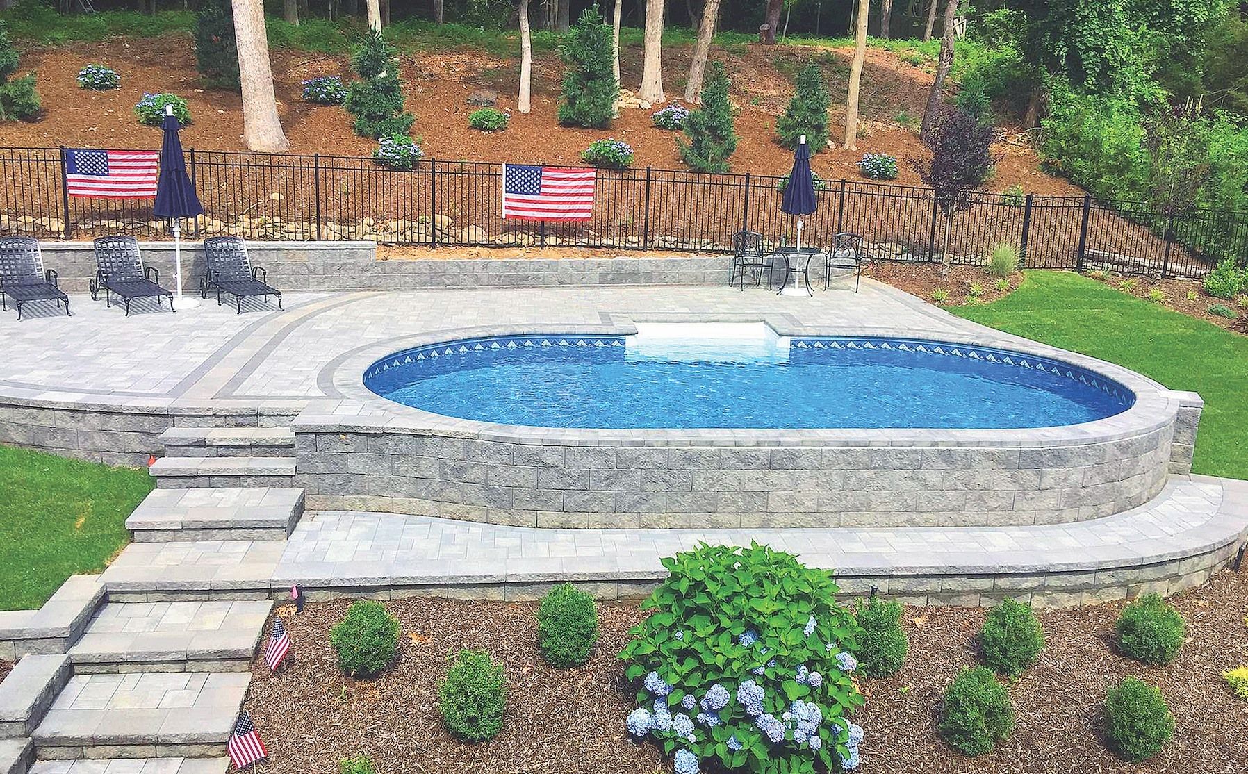 A large oval swimming pool is in the middle of a lush green yard.