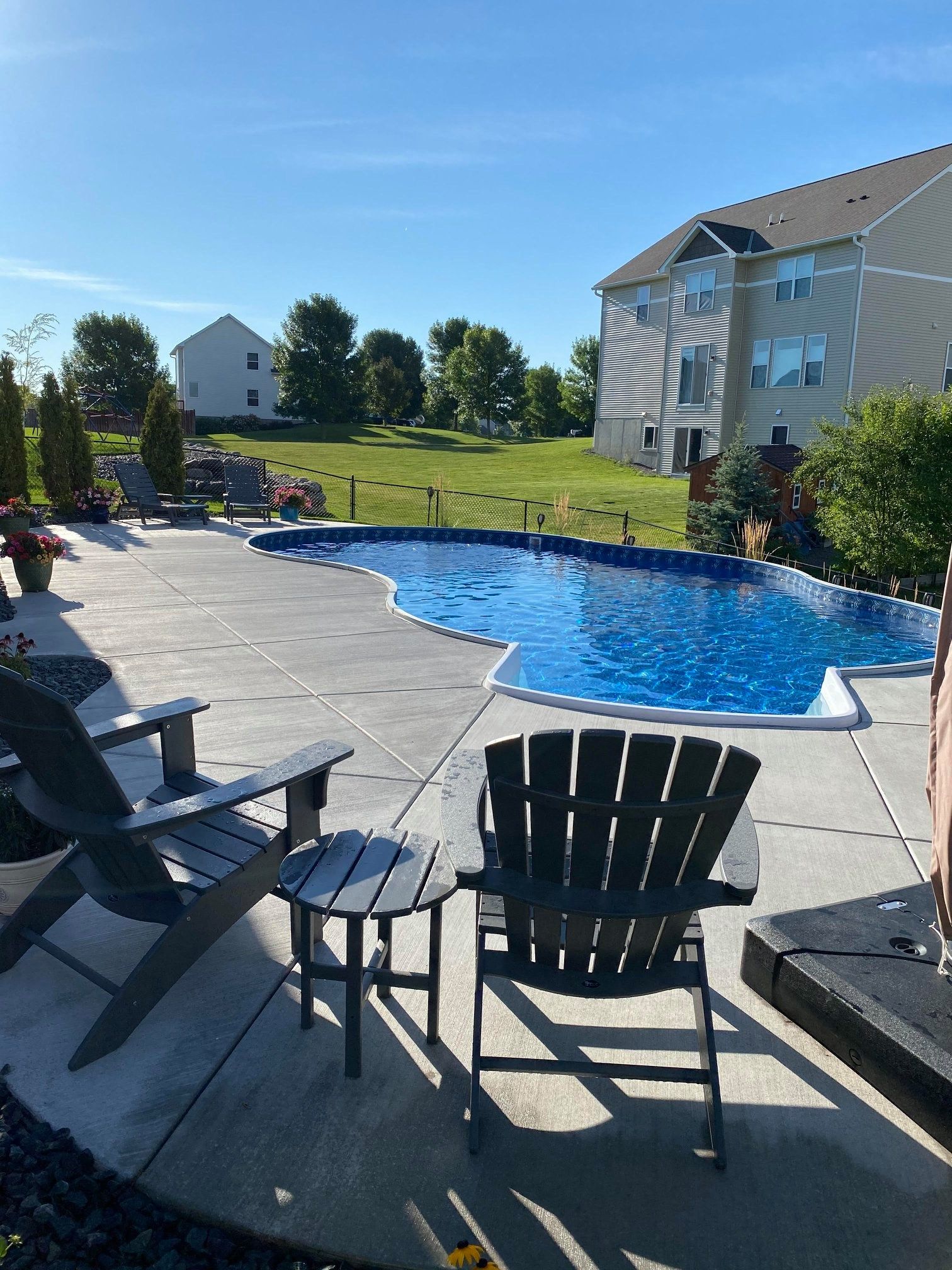 A patio with chairs and a table in front of a large swimming pool.