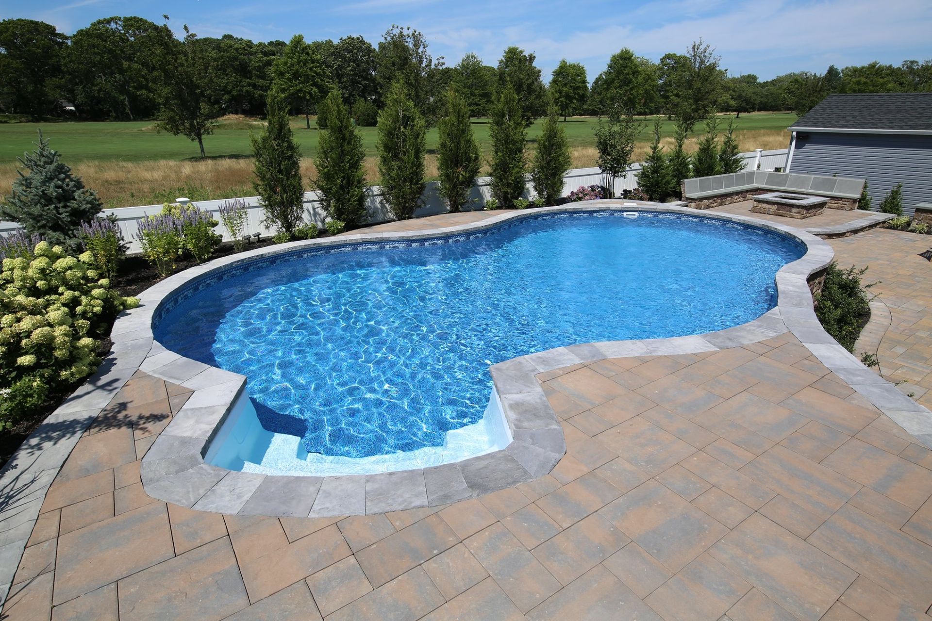 A large swimming pool is surrounded by a brick patio
