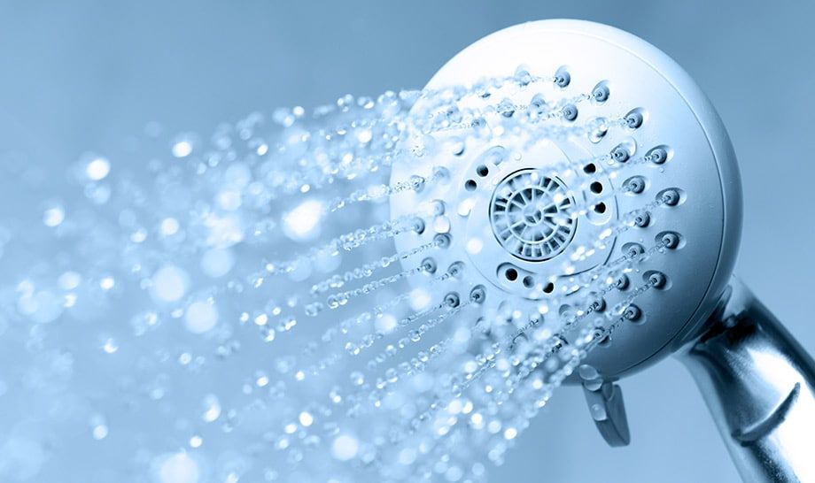 A close up of a shower head spraying water on a blue background.