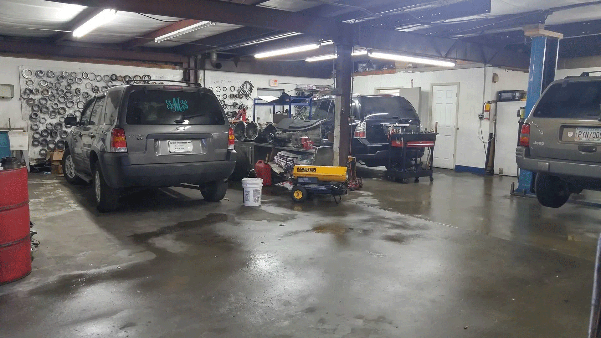 Dim auto repair garage with several parked vehicles and a wet concrete floor
