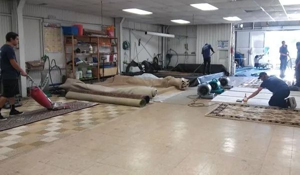 Workers installing rolled flooring in a large indoor room with tools and materials scattered around