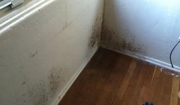 Empty corner of a room with scuffed white walls, dark wood floor, and a window ledge on the left.