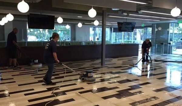People playing indoor hockey on a polished floor in a bright rink with large windows