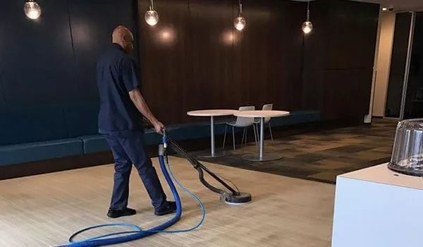 Worker vacuuming a dark lobby floor beside tables and wall lights