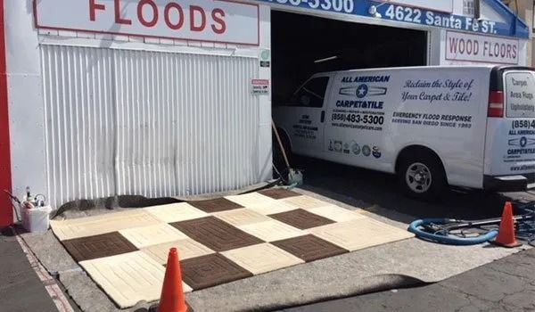 Floods storefront with a ramp to a moving truck, orange cones, and a checkered floor mat on the sidewalk