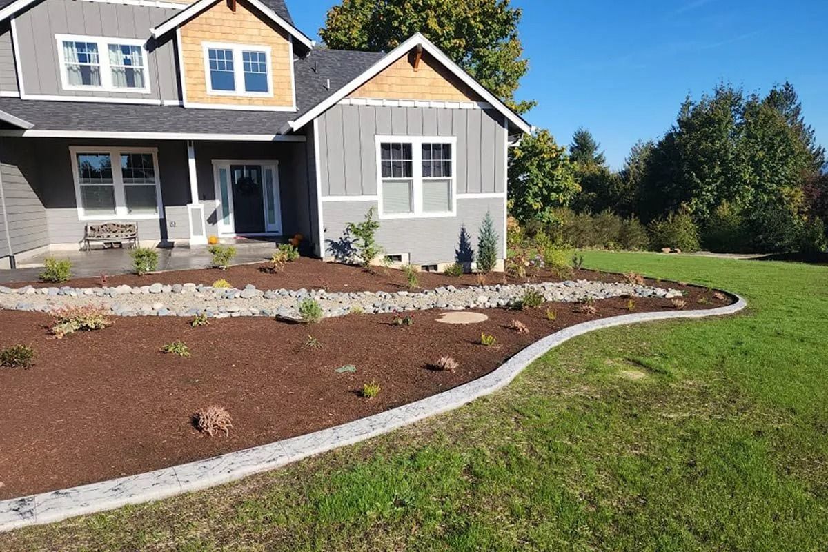 A gray two-story house with a newly landscaped front yard featuring a curved stone border, rock path, and mulch beds.