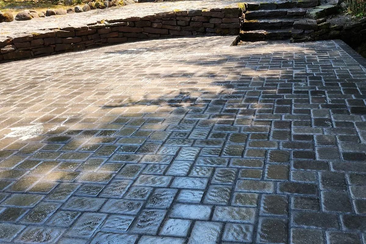 A patio made of grey, rectangular stone pavers, featuring a low retaining wall and stone steps leading to a higher level.