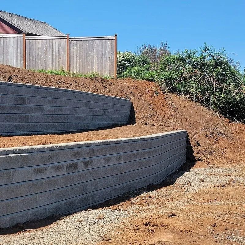 Two tiered gray concrete retaining walls built into a hillside below a wooden fence.
