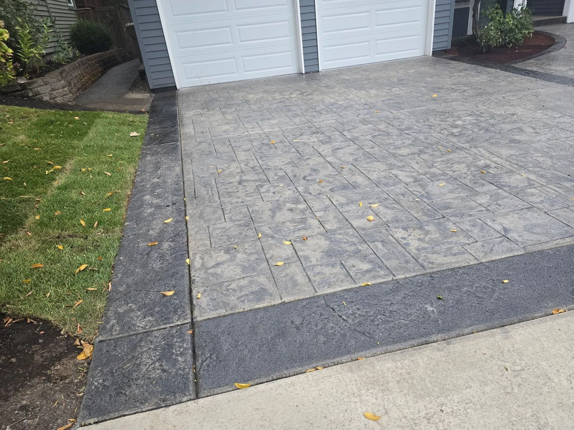 A stamped concrete driveway with a light grey patterned center section and dark grey border edges in front of a garage.