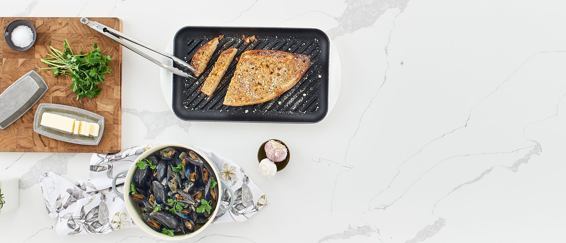 A white counter top with a pan of food and a bowl of mussels on it.