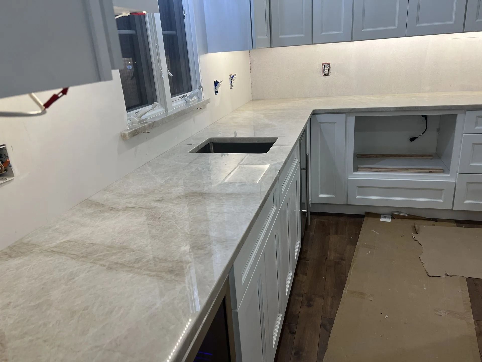 Kitchen with white cabinets, light stone countertop, sink, and unfinished floor under renovation.