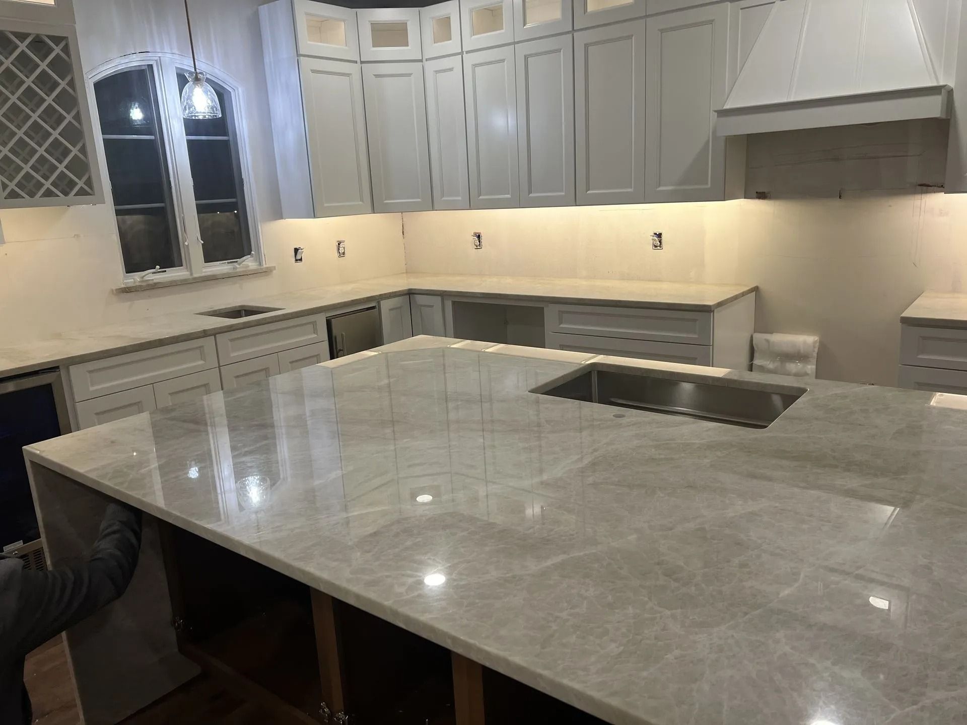 Modern kitchen with large gray marble island, white cabinets, and under-cabinet lighting